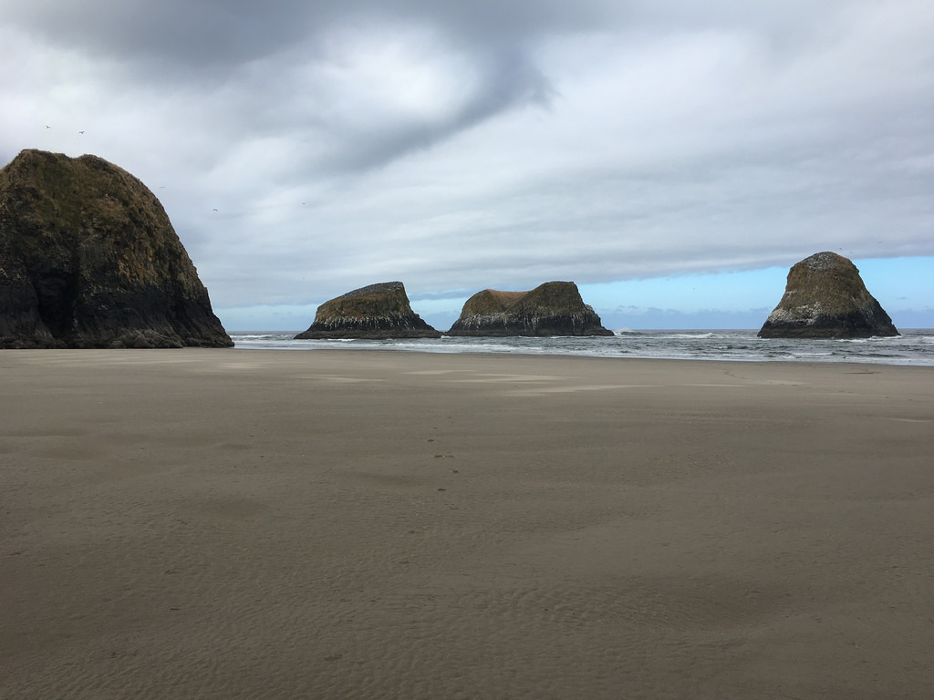 Four sea stacks, cloudy skies, and beach sand in the foreground