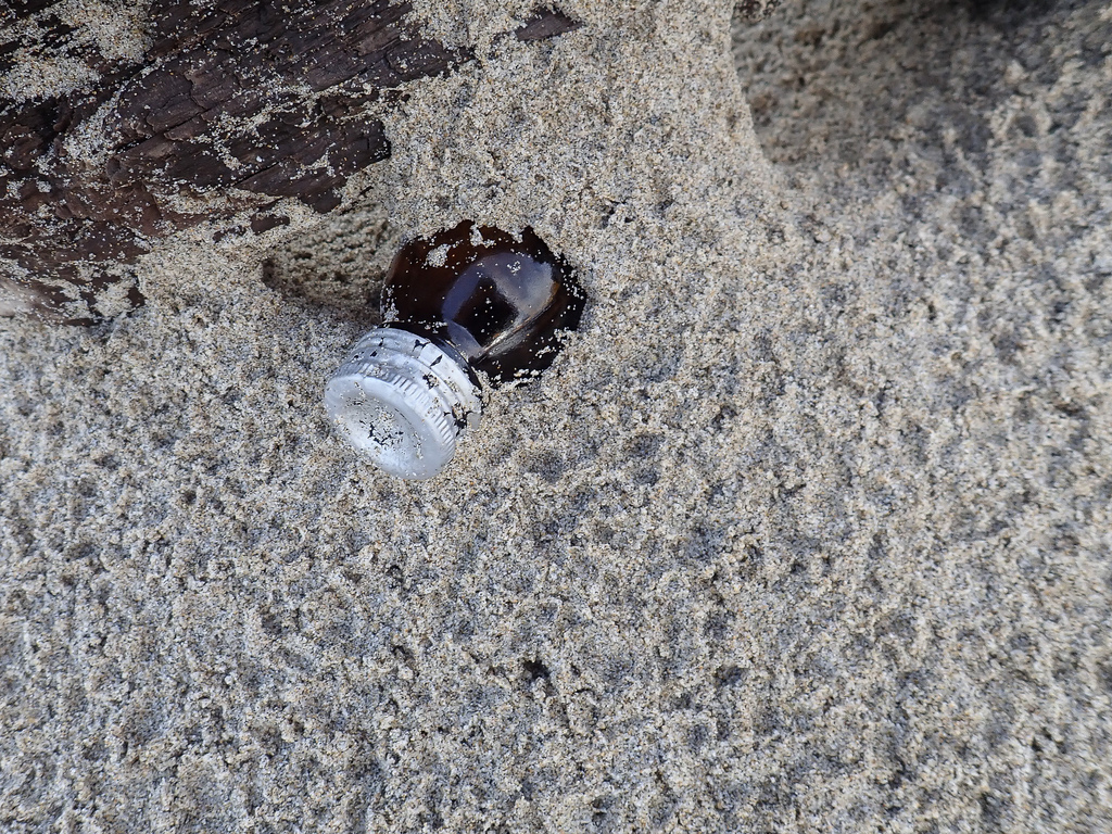 Small dark glass bottle mostly buried in sand