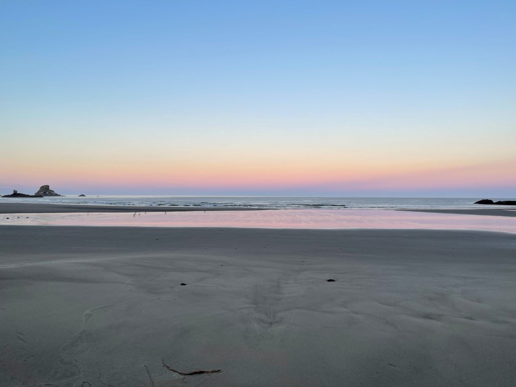 View out across the beach to the surf zone and beyond. Cloudless morning before sunrise, with a little color on the horizon