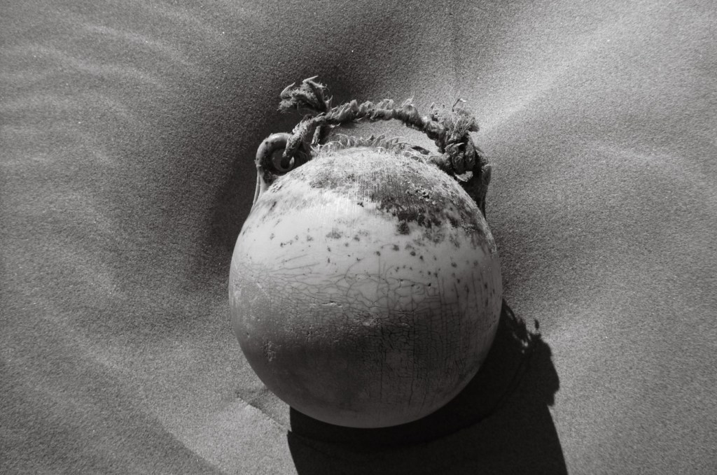 Old plastic buoy with sone frayed rope attached, on dry beach sand.