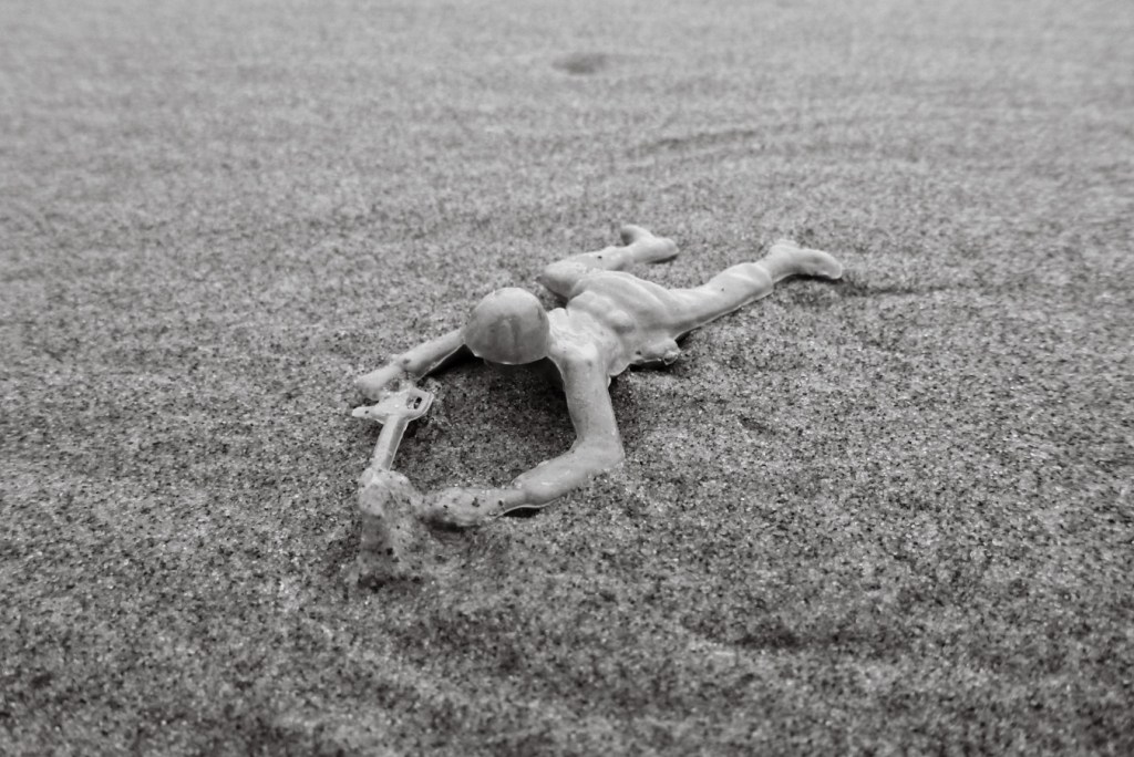 Plastic soldier figure, on beach sand in the prone position, crawling with a rifle
