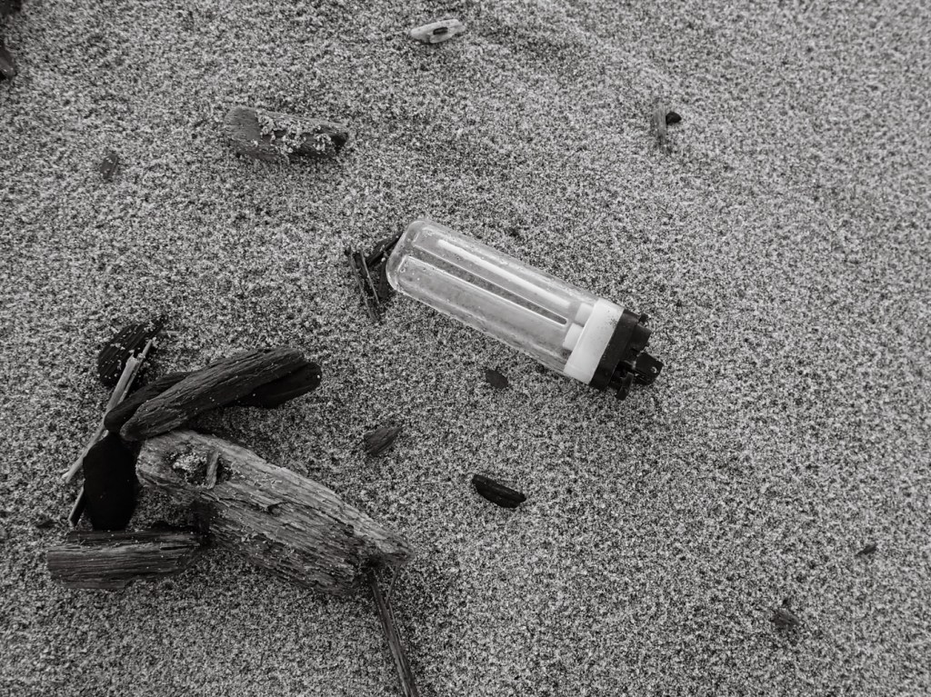 Plastic lighter on beach sand. The sand is dimpled with raindrops.