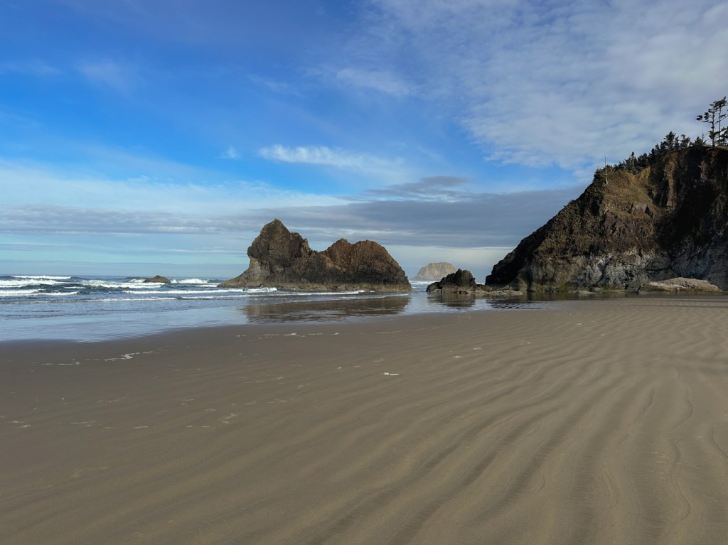 Rock formation in the surf zone. A sea stack in the distance. A few clouds.