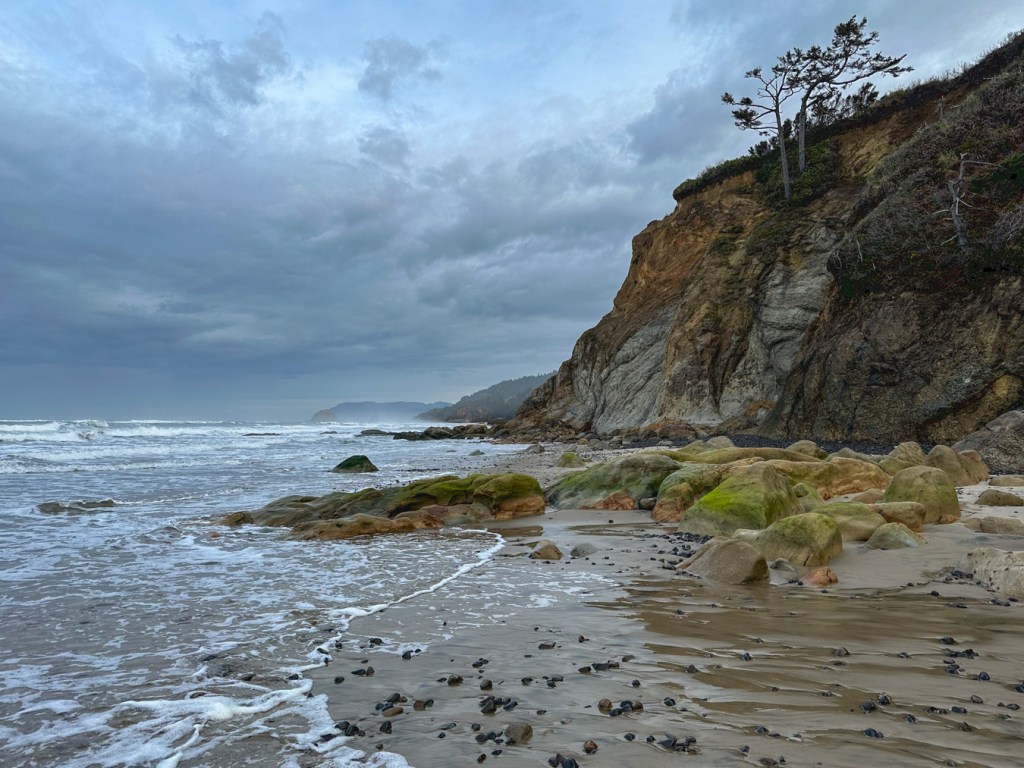 A cliff meets the surf. Cloudy sky.