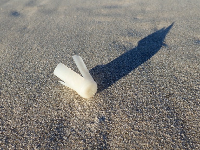 The wad from a shotgun shell casts a shadow on the sand.