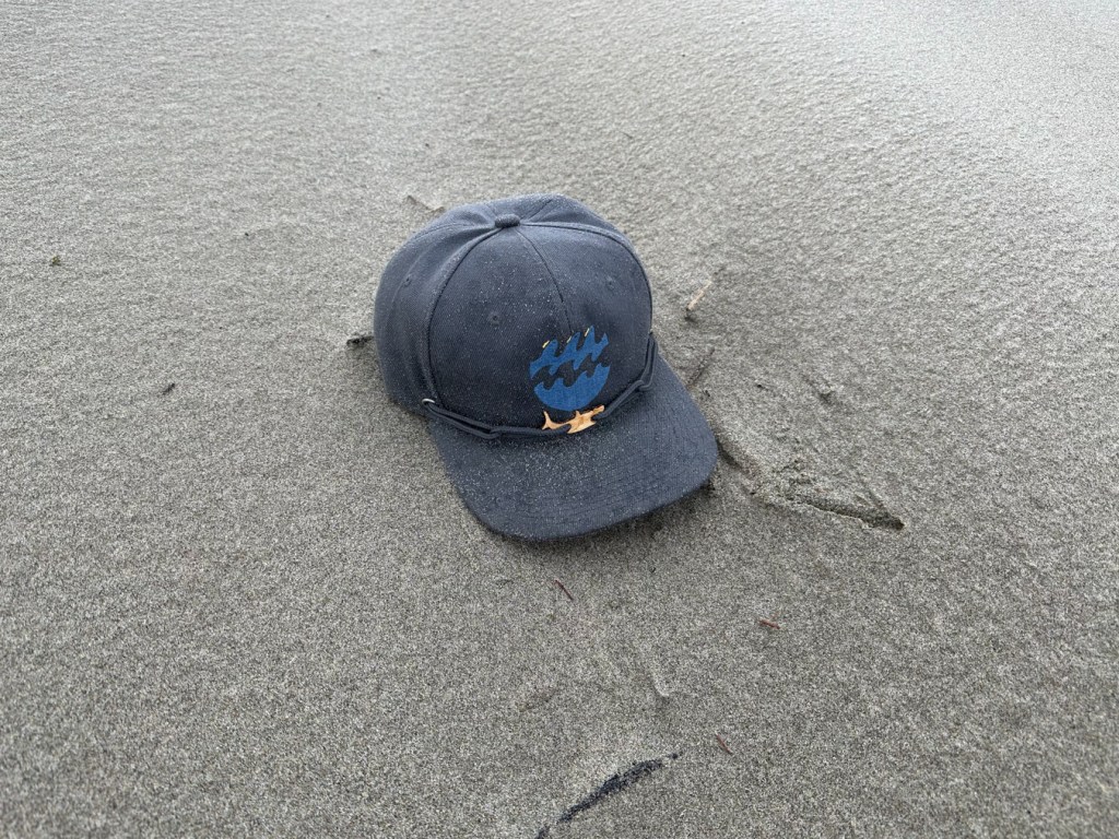 A hat, darkened in places by a few raindrops rests on the sand.