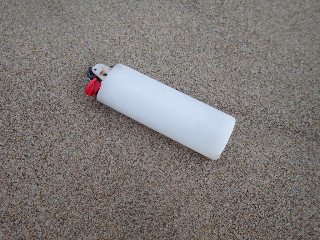 A disposable lighter rests on the sand.