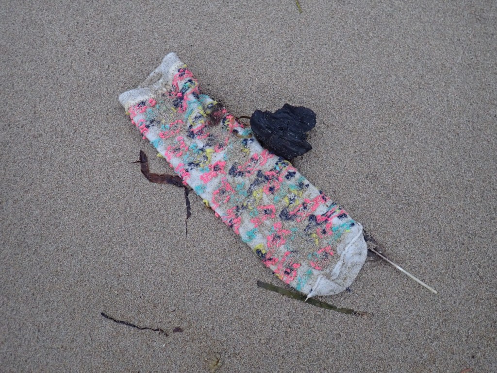 A kid's lost sock rests on the sand.