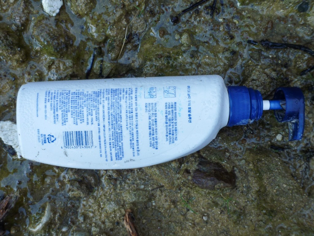 Closeup of a plastic pump bottle, maybe lotion, resting in the cobbles.