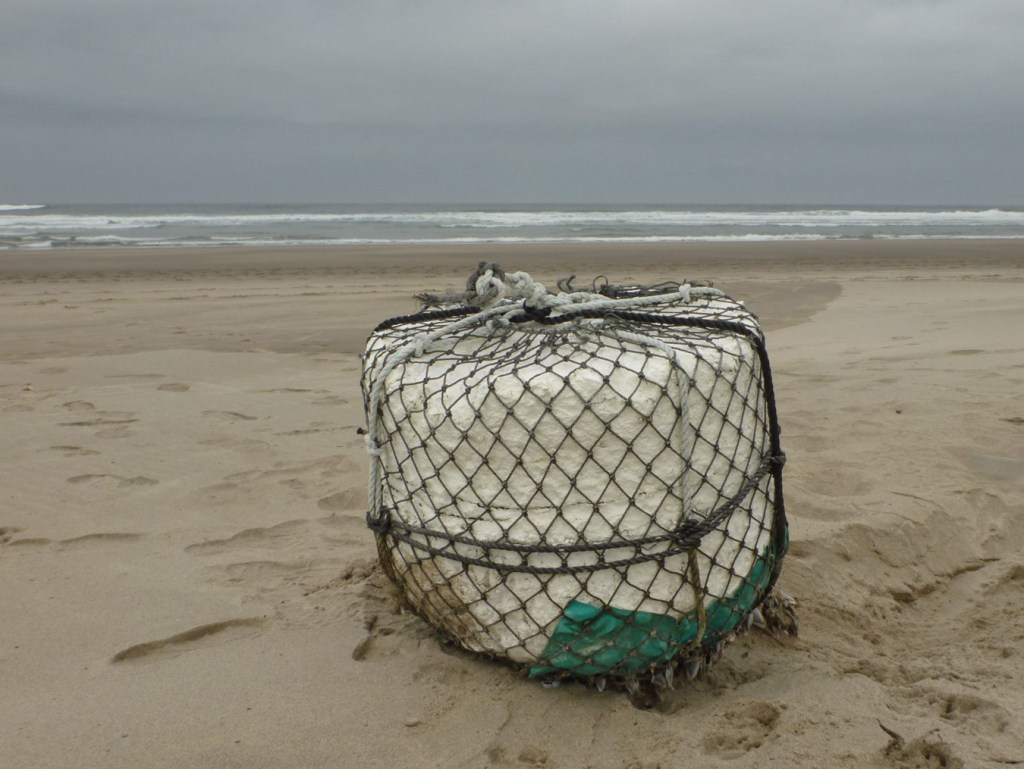 A lost do-it-yourself buoy rests on the beach. Surf zone in the distance. Cloudy sky.