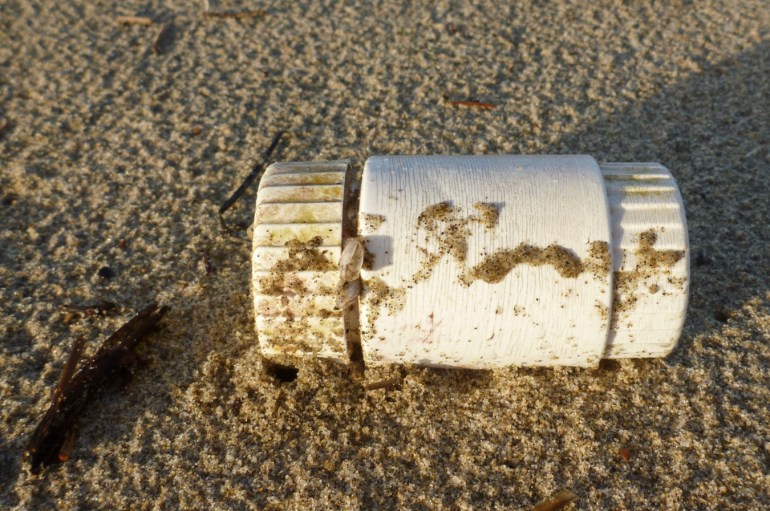 A plastic pill bottle rests on rain-dimpled sand.