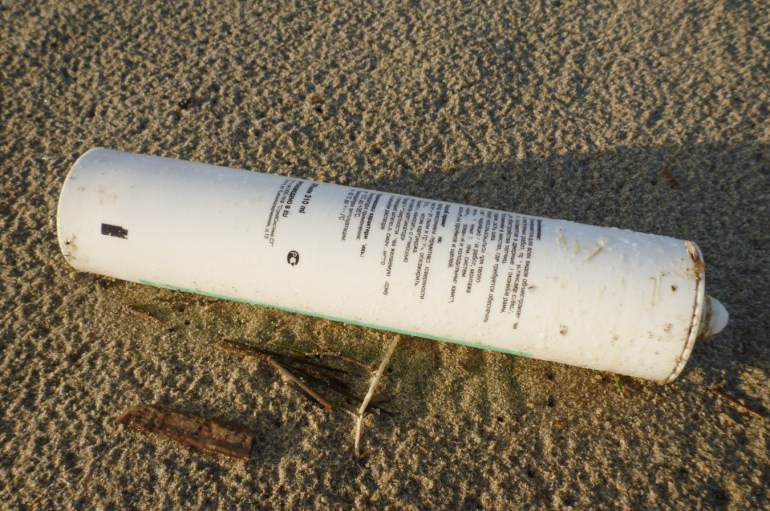 Silicon applicator tube in a language I can't read resting on rain-dimpled sand.