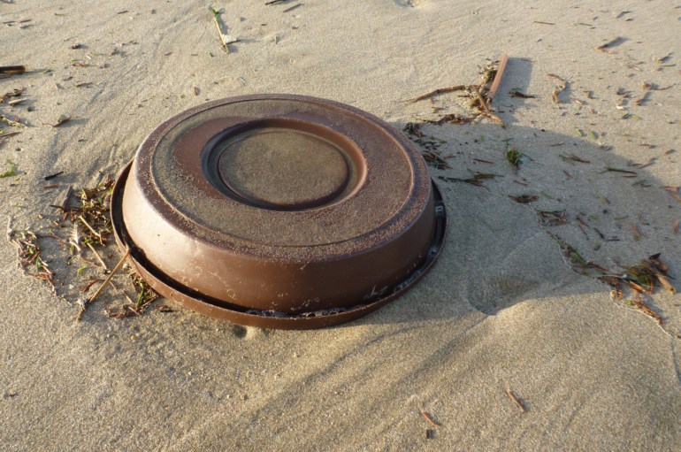 Plastic dog bowl resting upside down on the sand.
