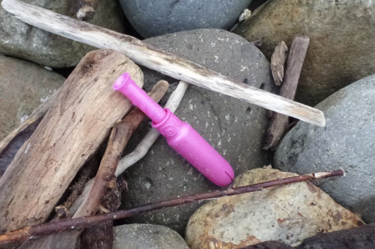 A disposable plastic tampon applicator rests on the cobbles with some small driftwood.