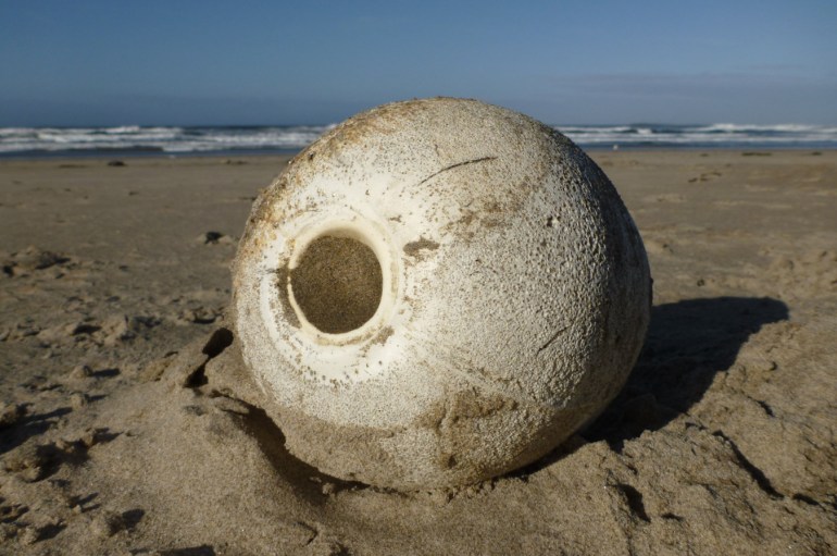 A roundish polystyrene float with a central plastic-lined hole rests on the beach. Beach and surf zone in the background. Clear sunny sky.A roundish polystyrene float with a central plastic-lined hole rests on the beach. Beach and surf zone in the background. Clear sunny sky