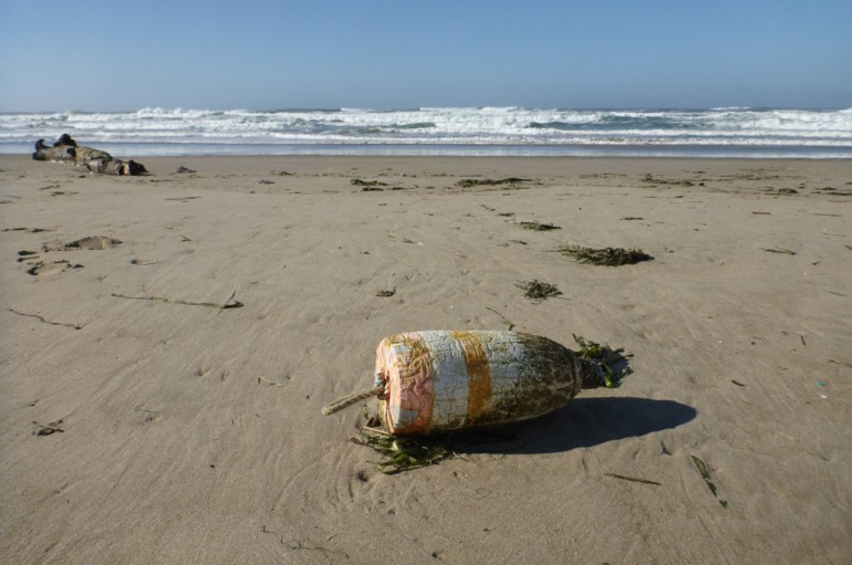 A lost marker buoy rests on the sand. Beach and surf zone in the background. Clear sunny sky.
