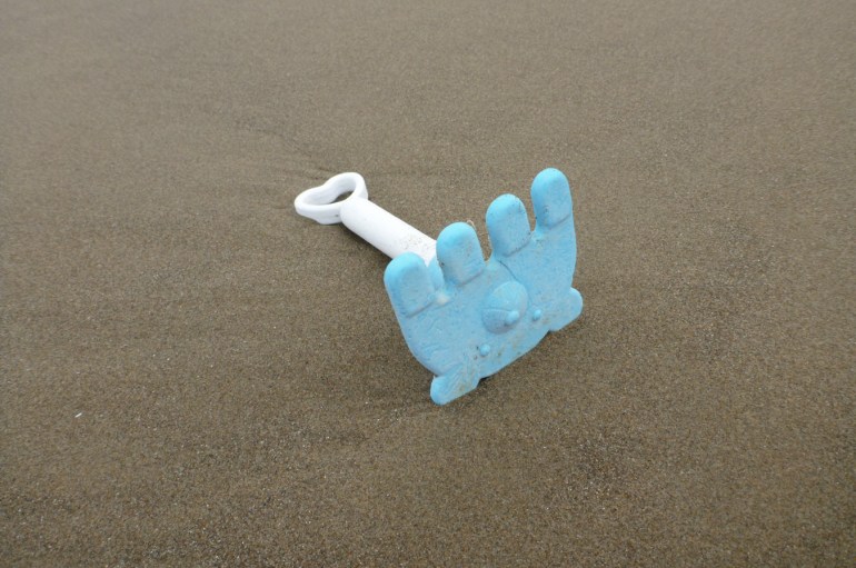 A lost child's sandbox rake with the rake part resembling a foot with four toes rests on the sand.