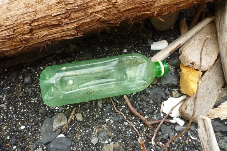 A empty and drifted plastic bottle rests among driftwood and styrofoam debris.