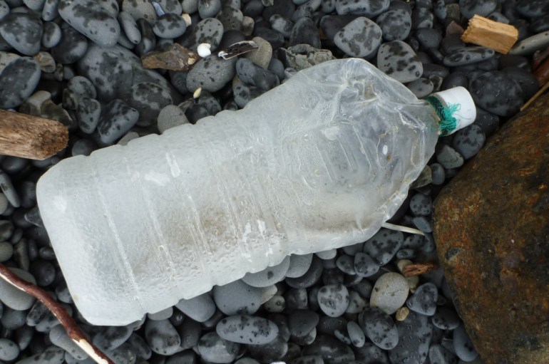 A lost and drifted DIY float made from a large empty plastic bottle rests in the cobbles.
