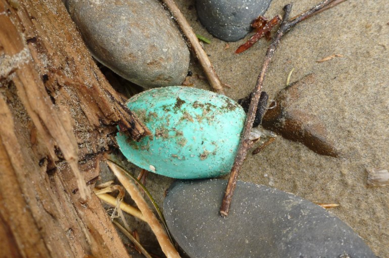 A lost and drifted football-shaped float rests on the sand among driftwood and cobbles.