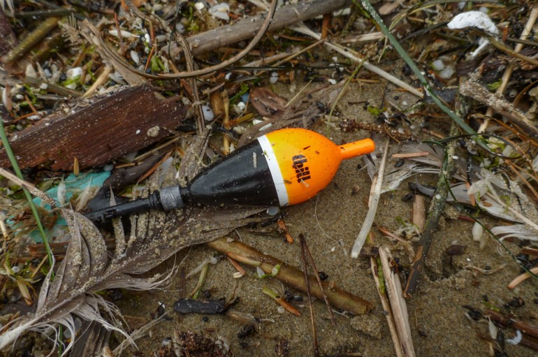 A lost and drifted float (Thill float, steelhead gear) rests on the sand among other drifted debris.