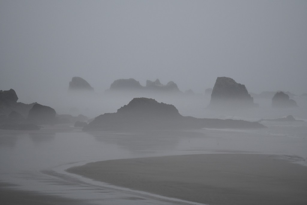 Rocks and seas stacks poking up above the mist. Beach in the foreground.