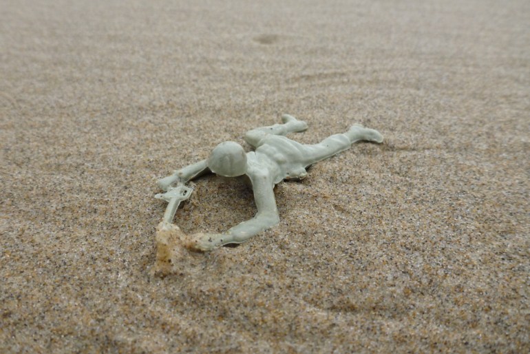 Plastic toy soldier resting on the sand.