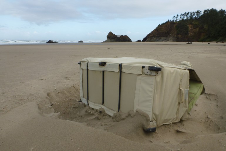 A lost and drifted wheelie bed rests on the sand.
