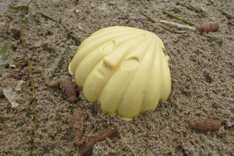 A lost plastic seashell rests on the sand.