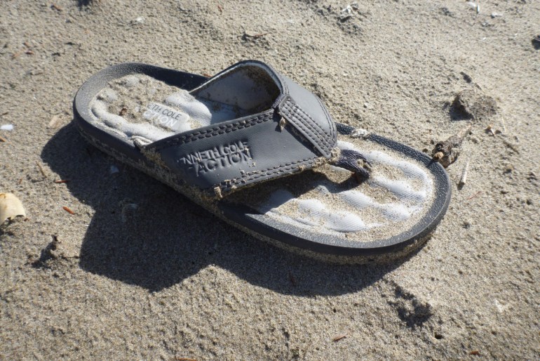 A lost and drifted flip flop rests on the sand.