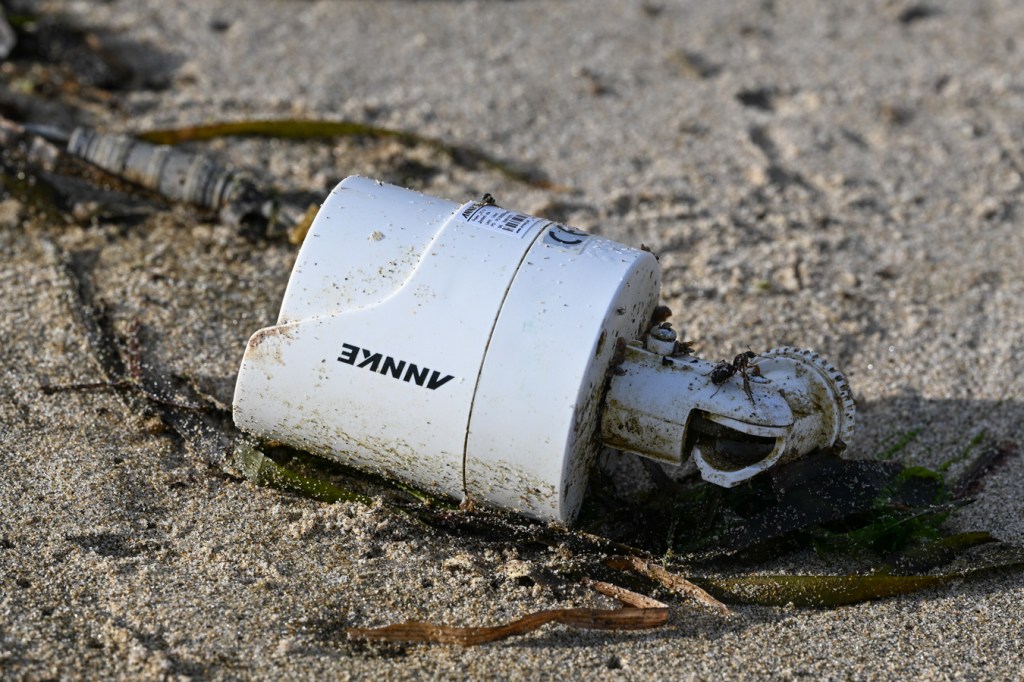 A lost and drifted surveillance camera rests on the sand among blades of drifted eelgrass (Zostera).