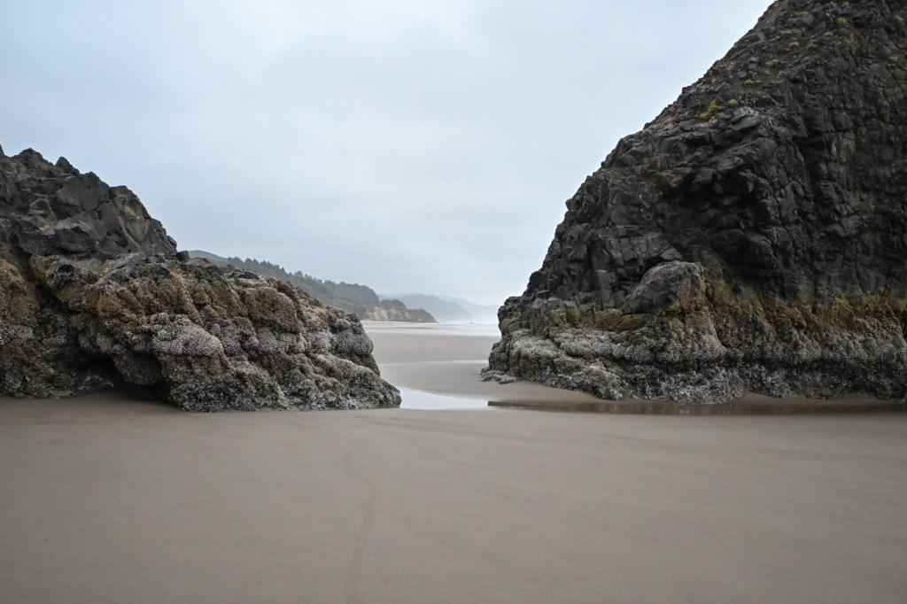 A seascape showing the view south through a gap in the rocks, along the beach to a series of distant headlands.