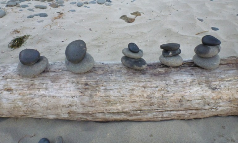 Five cobble cairns on a drift log on the sand.