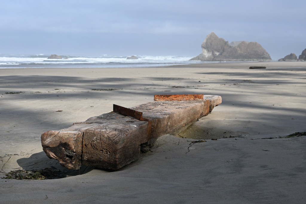Two heavy timbers connected by rusting angle irons rest on the sand.