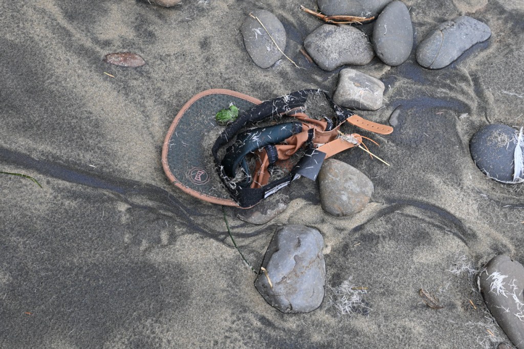 A beached Melin hat rests in a heap high on the beach at the interface of sand and cobbles.