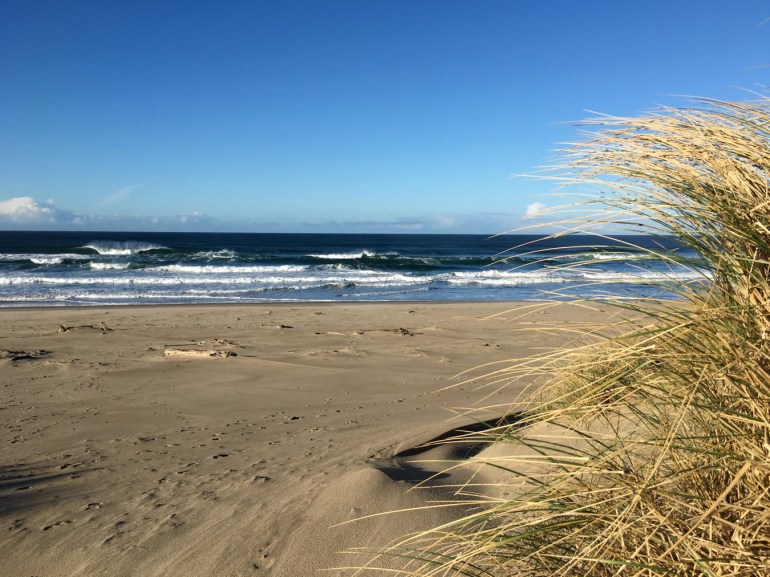 A beachscape with the surf zone in the middle distance and a few clouds out on the horizon.