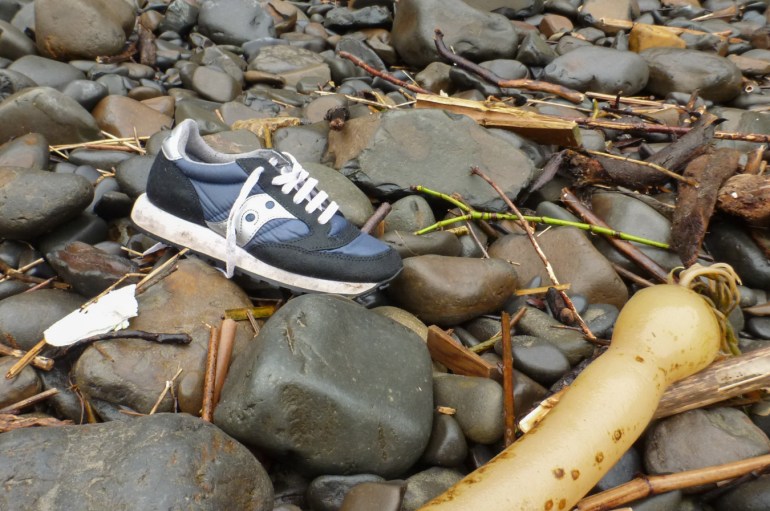 A lost sneaker rests in the cobbles along with other wrack line debris.