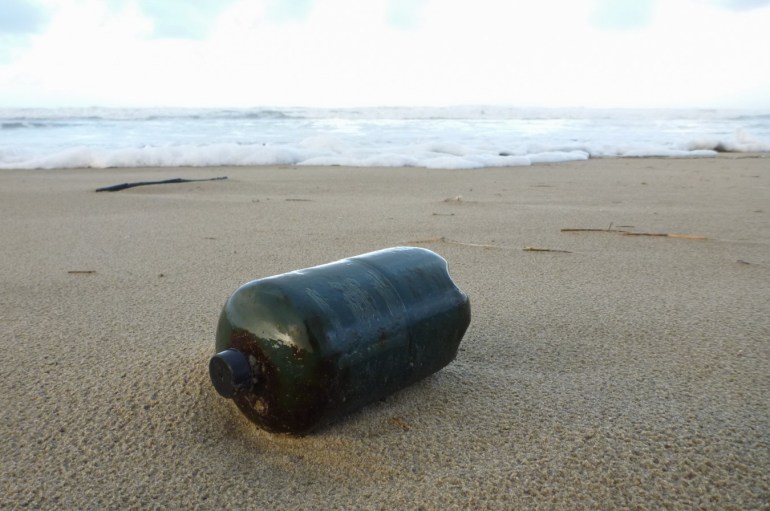 A small propane fuel canister rests on rain-dimpled sand just above the swash.