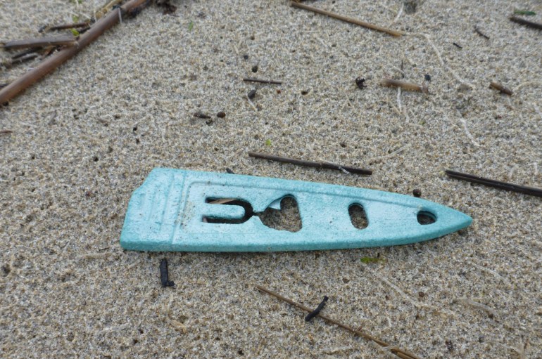 A lost and drifted knife sheath rests on rain-dimpled sand.